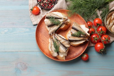 Delicious sandwiches with sprats and dill served on light blue wooden table, top view