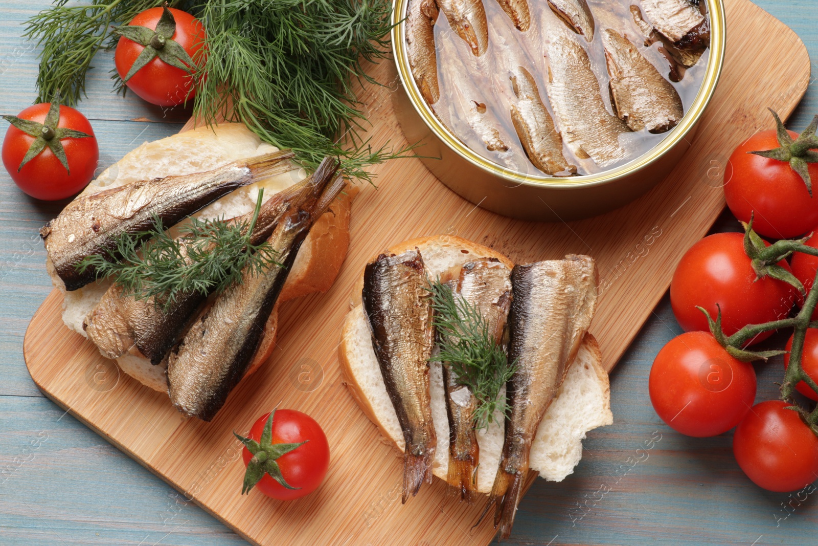 Photo of Delicious sandwiches with sprats and dill served on light blue wooden table, top view