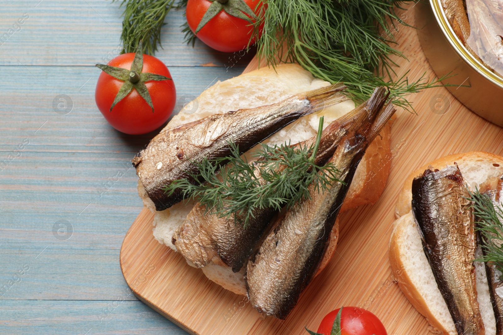 Photo of Delicious sandwiches with sprats, dill and tomatoes on light blue wooden table, top view