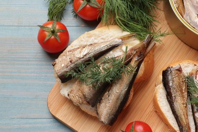 Photo of Delicious sandwiches with sprats, dill and tomatoes on light blue wooden table, top view