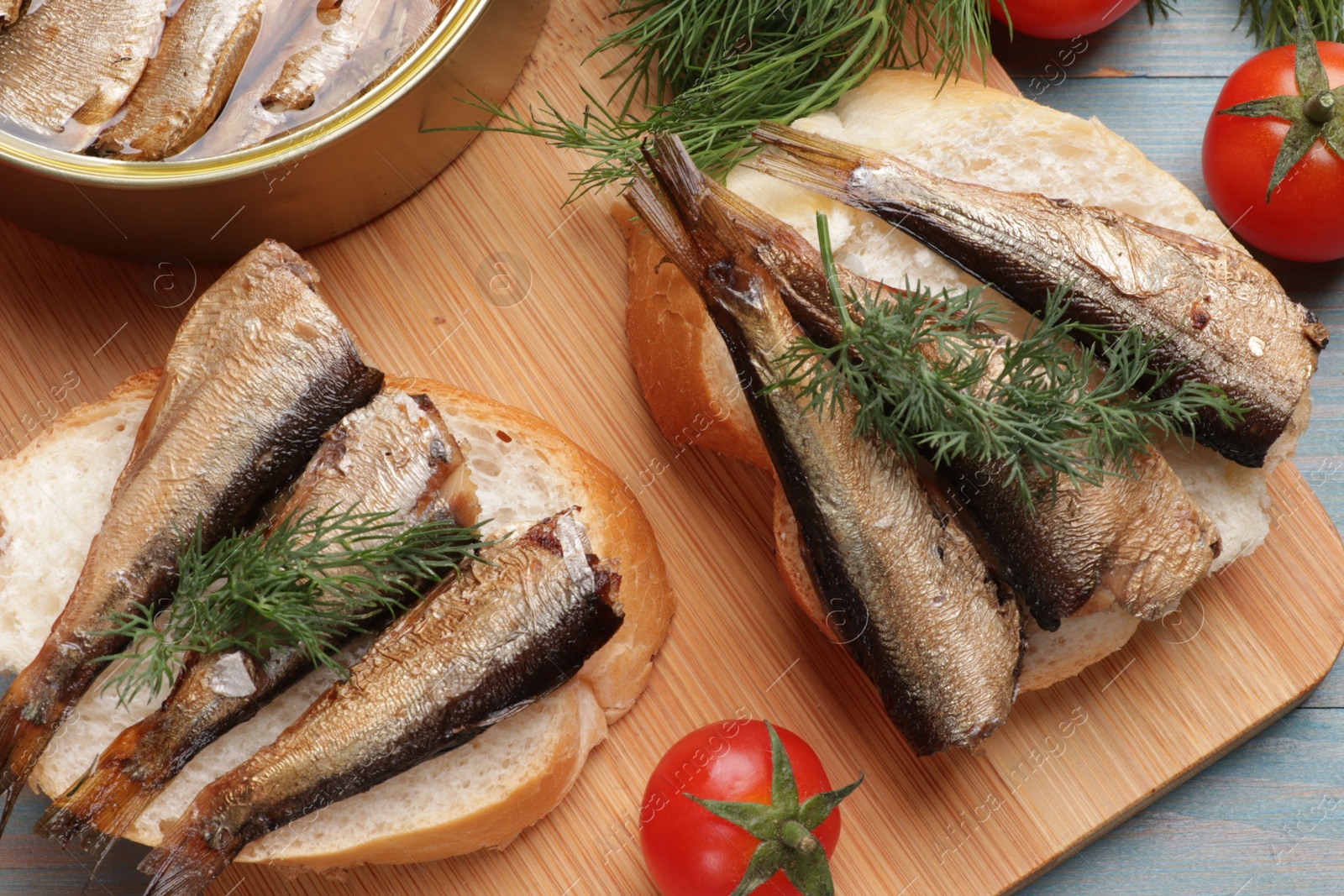 Photo of Delicious sandwiches with sprats and dill served on light blue wooden table, top view