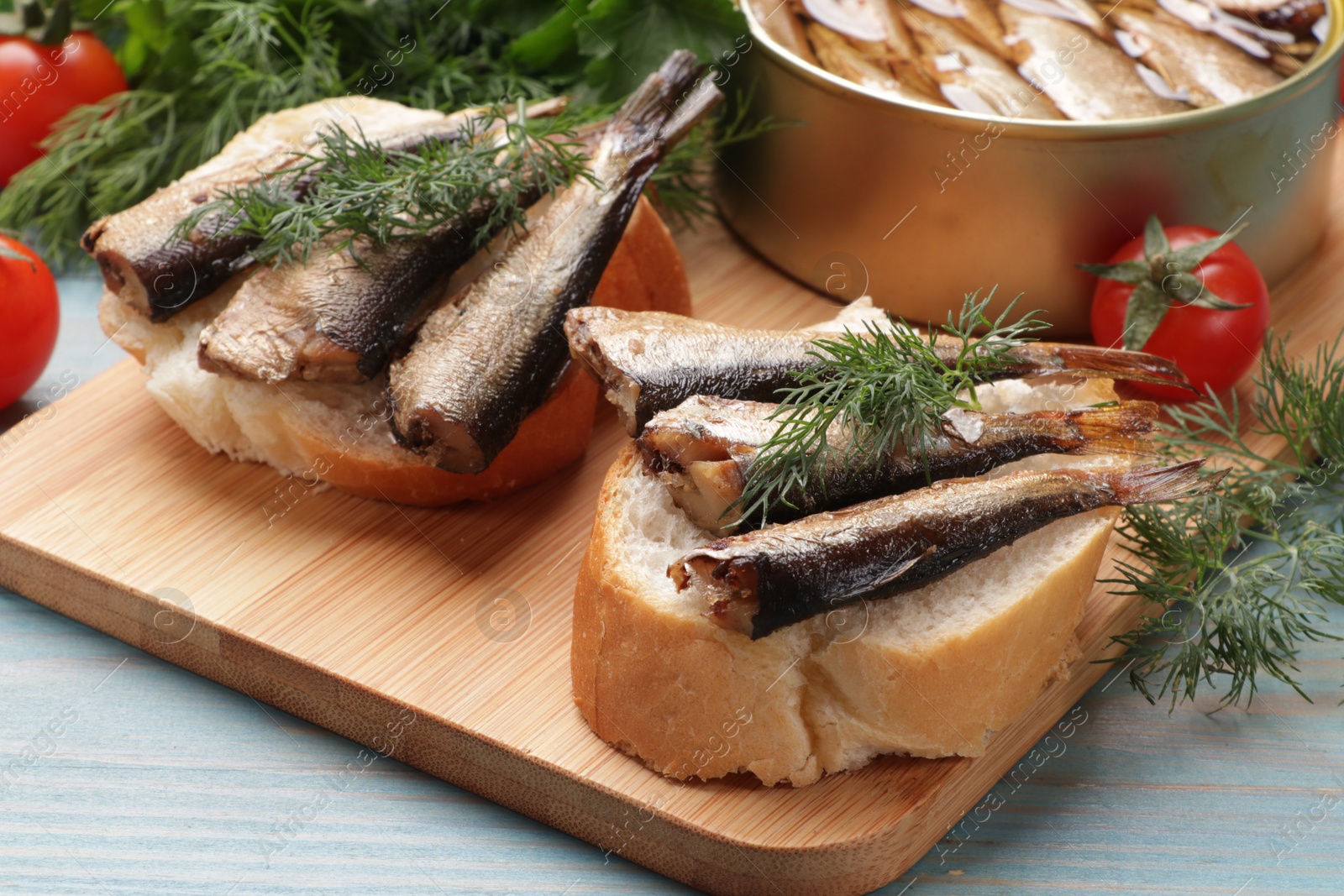 Photo of Delicious sandwiches with sprats and dill served on light blue wooden table, closeup