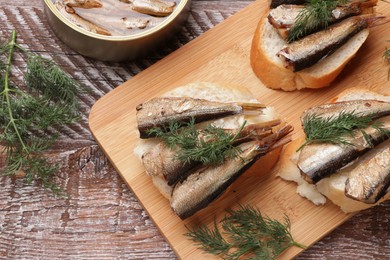 Delicious sandwiches with sprats and dill on wooden table, top view