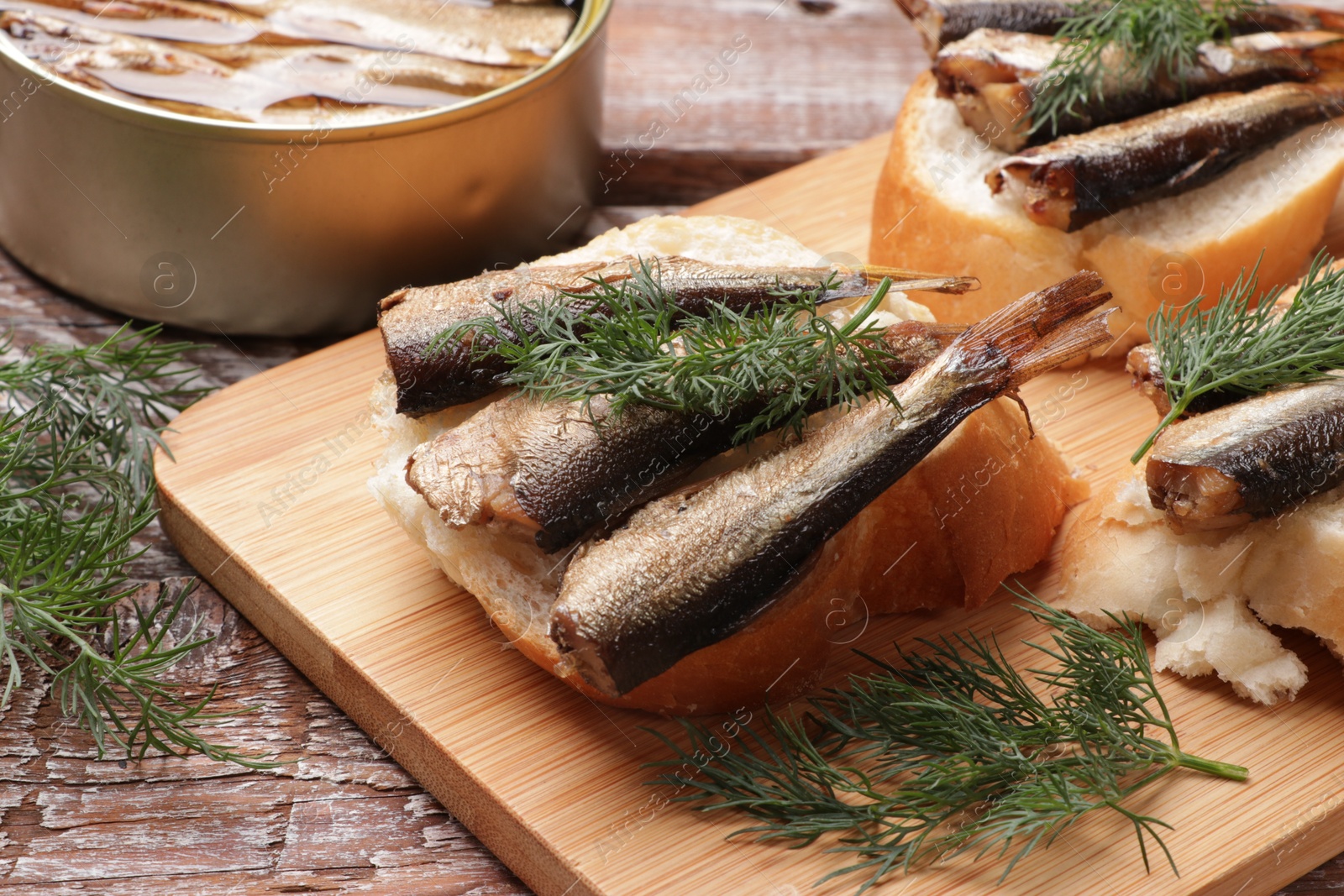 Photo of Delicious sandwiches with sprats and dill on wooden table, closeup