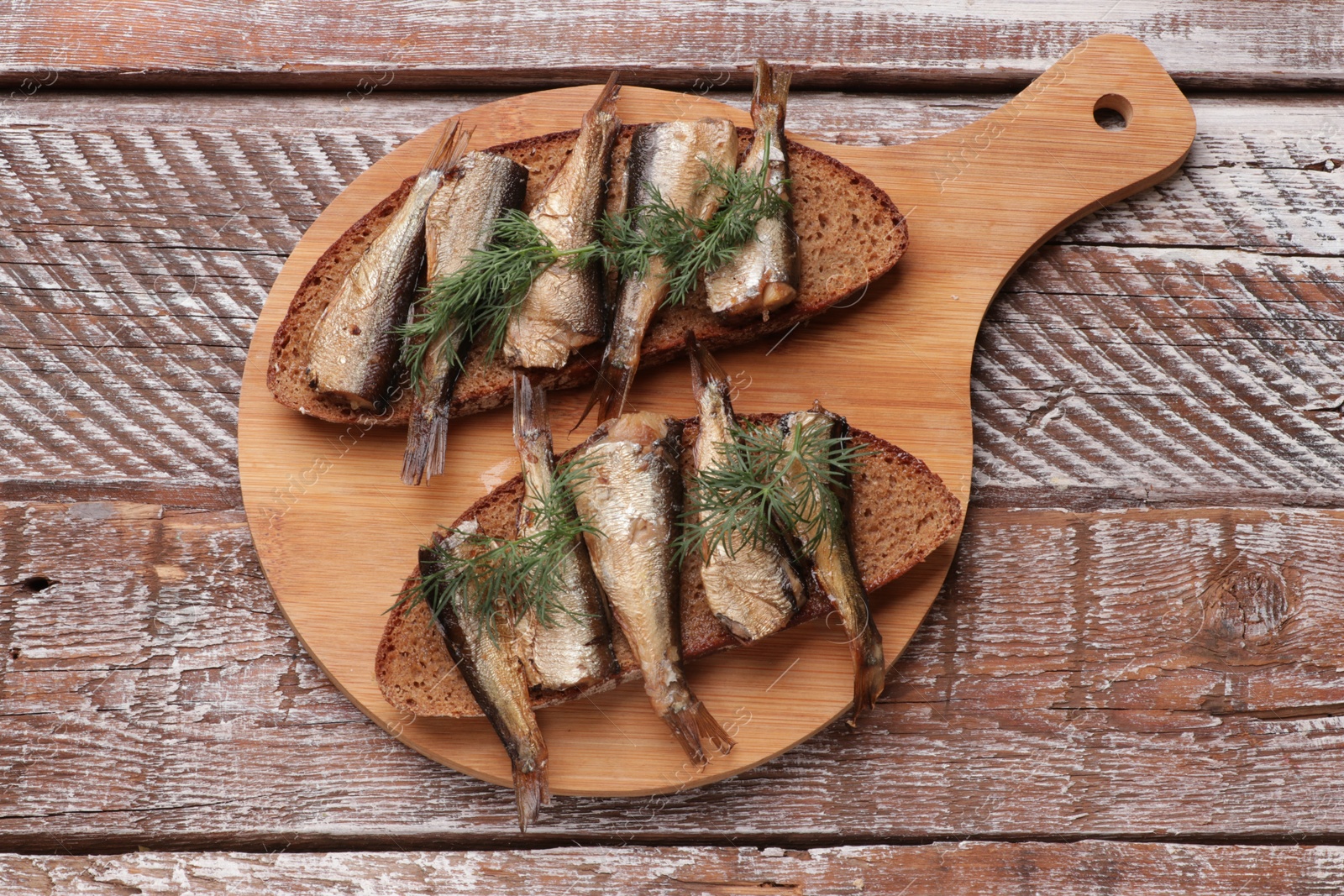 Photo of Delicious sandwiches with sprats and dill on wooden table, top view