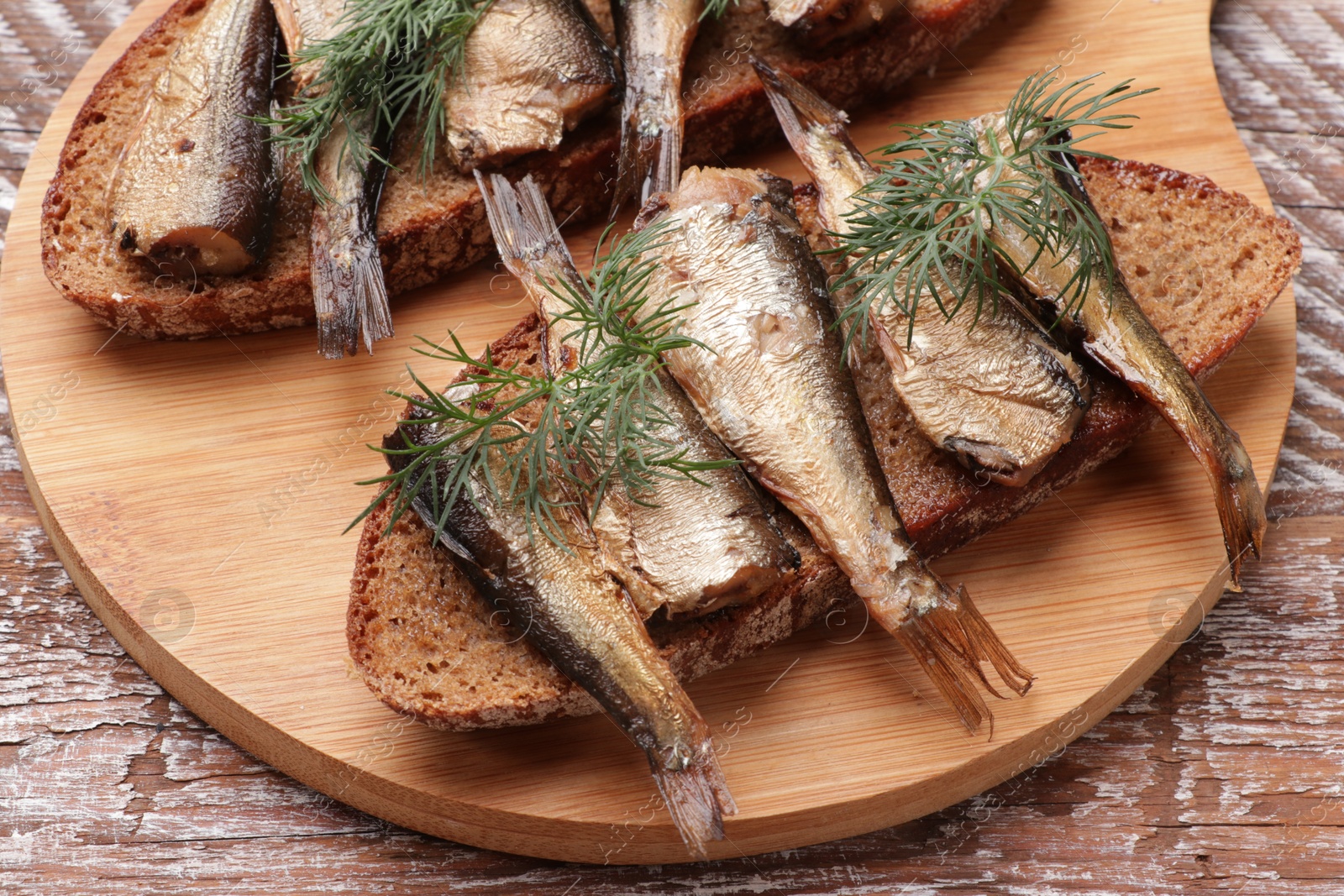 Photo of Delicious sandwiches with sprats and dill on wooden table, closeup