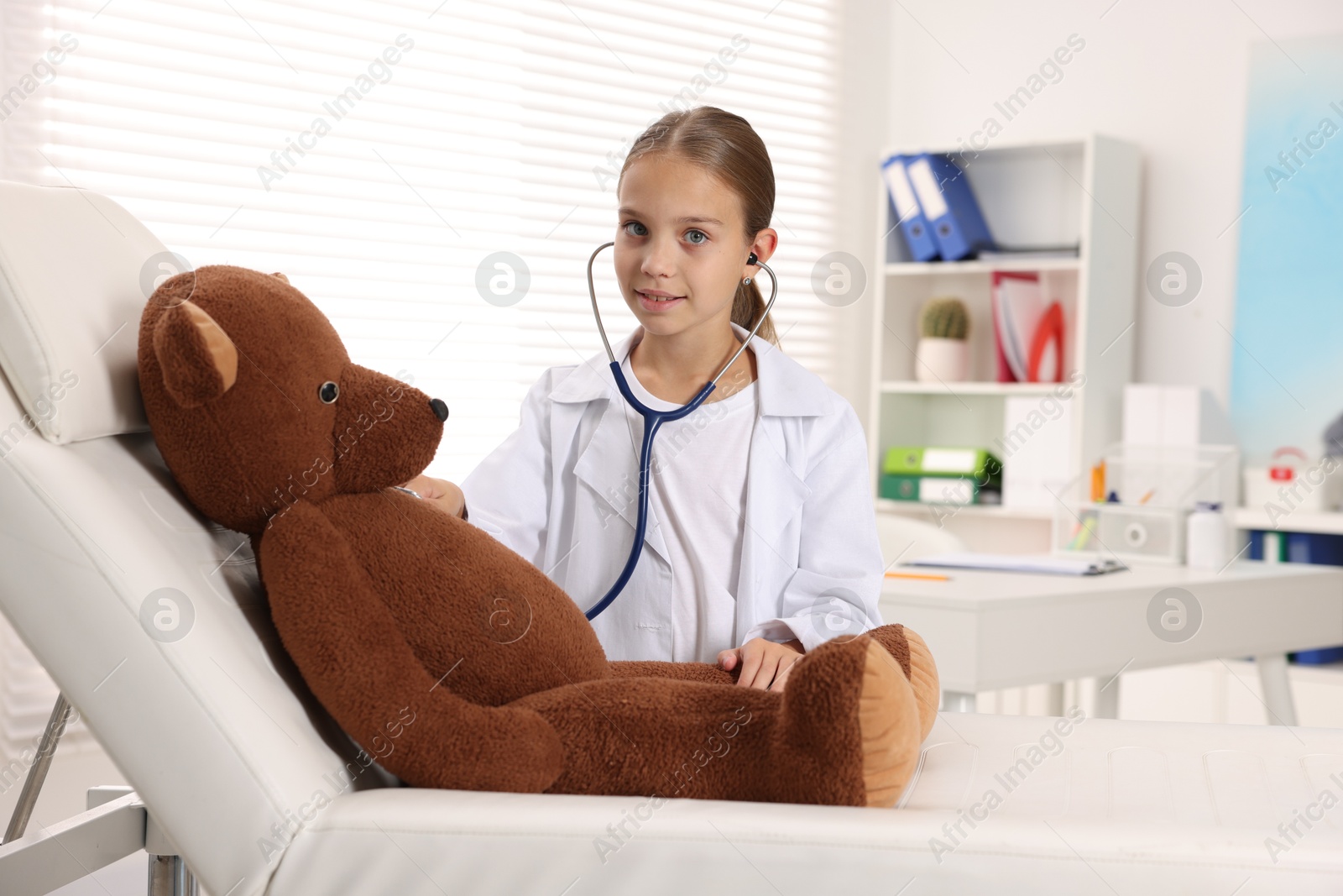 Photo of Girl with stethoscope and toy pretending to be doctor indoors