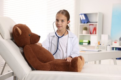 Photo of Girl with stethoscope and toy pretending to be doctor indoors