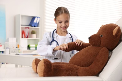 Photo of Girl with stethoscope and toy pretending to be doctor indoors