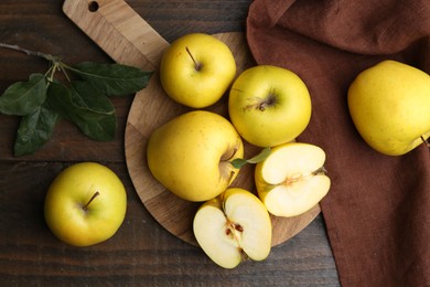 Fresh ripe yellow apples and green leaves on wooden table, flat lay