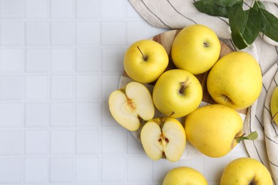 Fresh ripe yellow apples and leaves on white tiled table, flat lay. Space for text