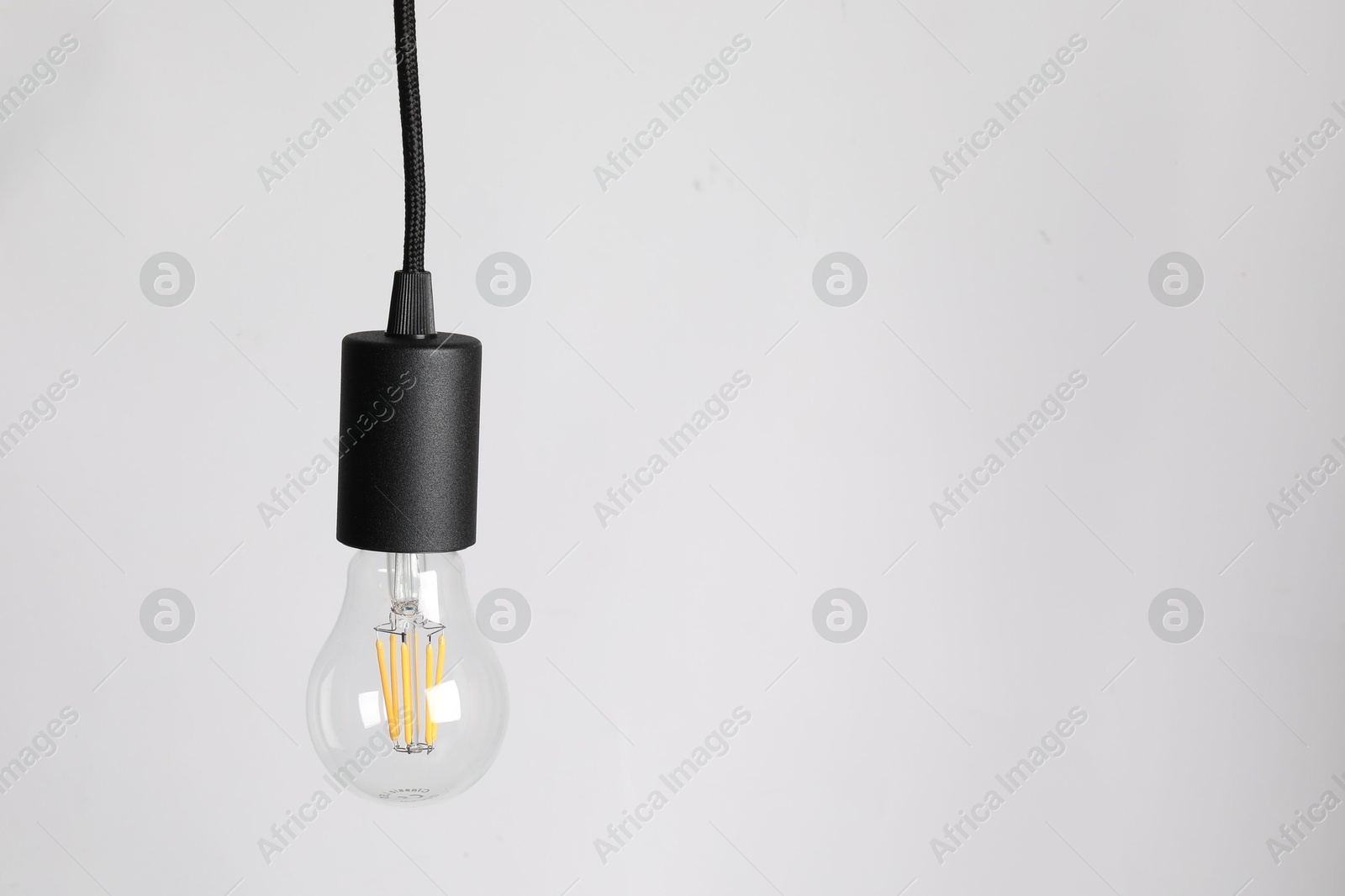 Photo of One light bulb hanging on cord against white background. Space for text