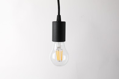 Photo of One light bulb hanging on cord against white background