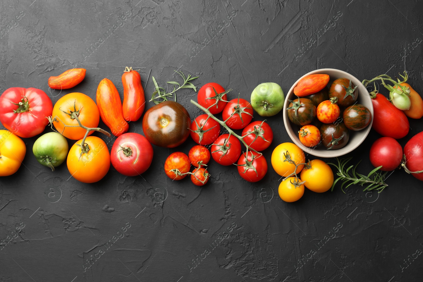 Photo of Different fresh tomatoes and rosemary on grey textured table, flat lay