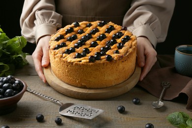 Photo of Woman with homemade blueberry pie at wooden table, closeup