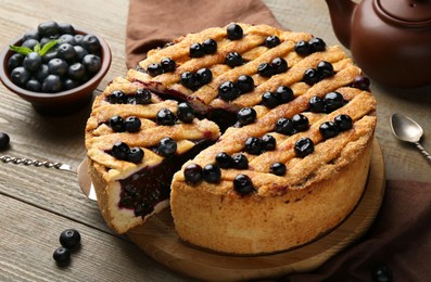 Photo of Taking slice of homemade blueberry pie and fresh berries on wooden table, closeup