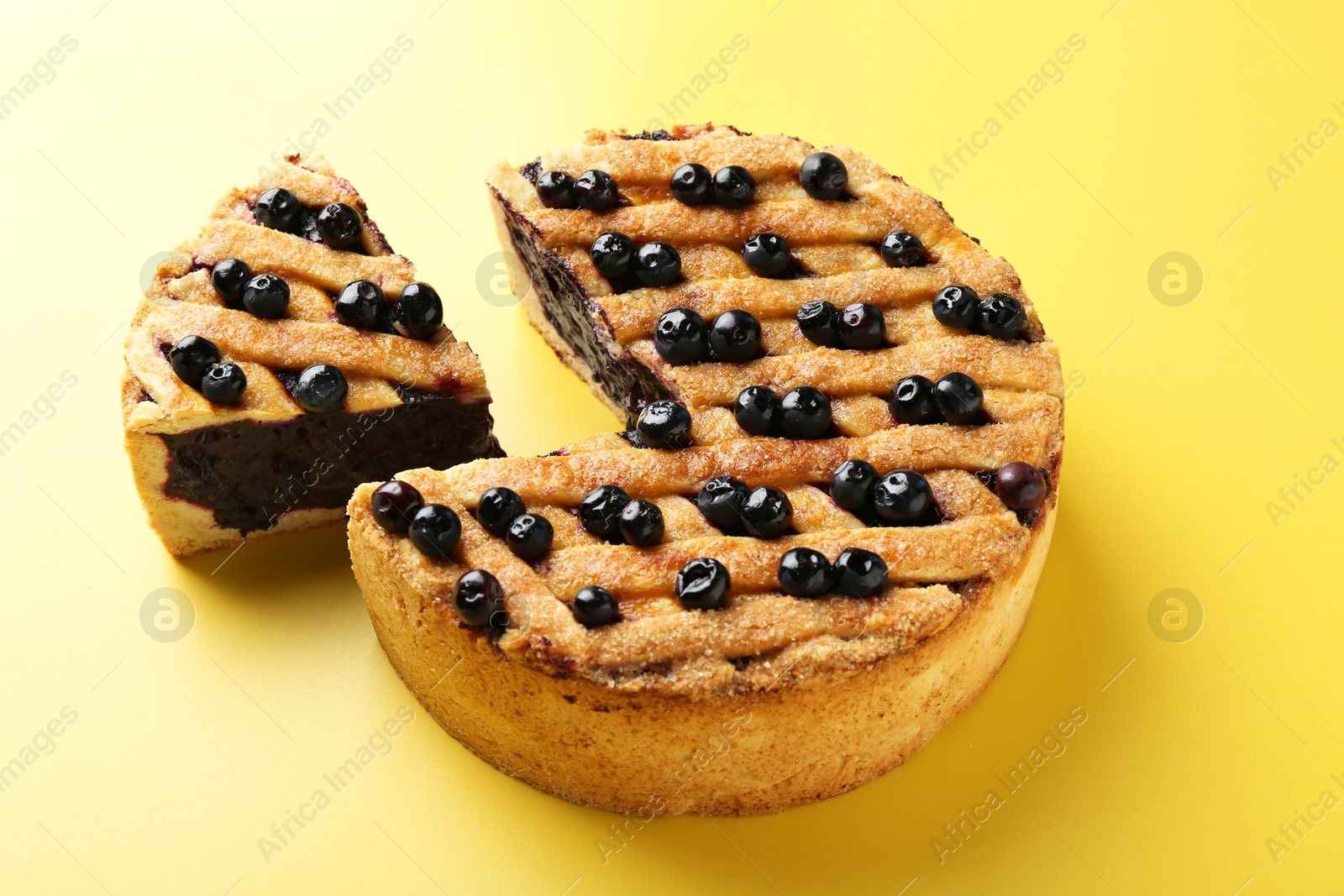 Photo of Cut homemade blueberry pie on yellow background