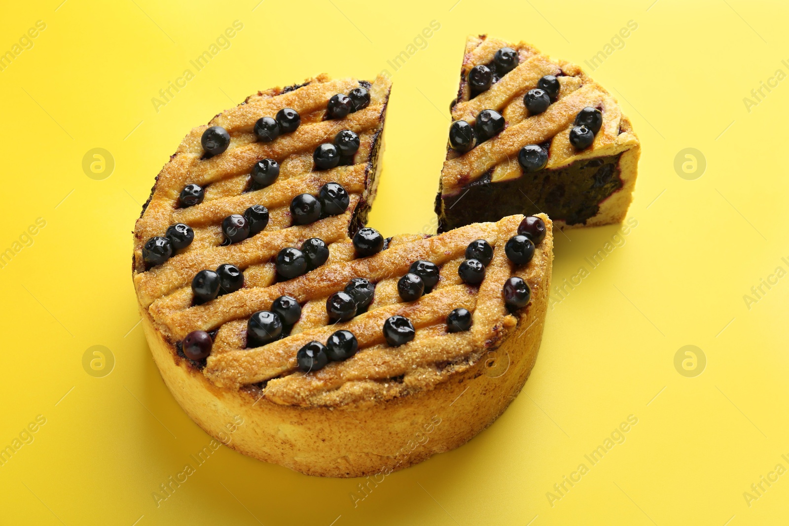 Photo of Cut homemade blueberry pie on yellow background