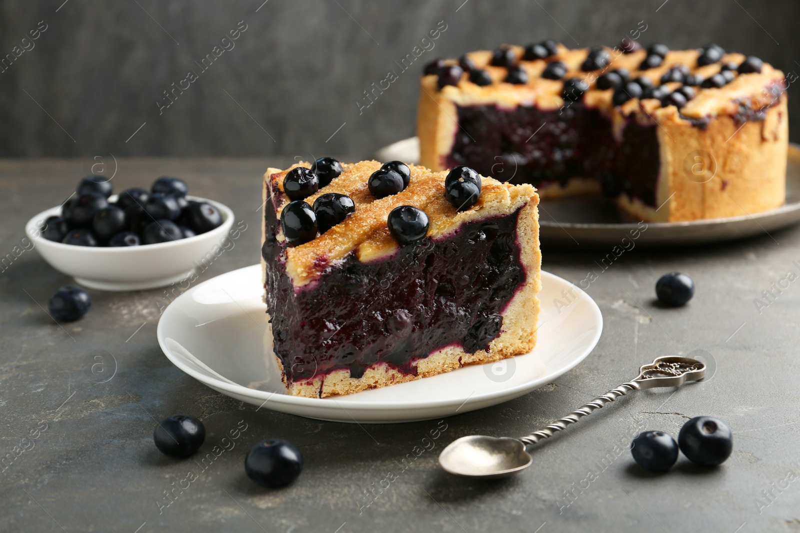 Photo of Slice of delicious homemade blueberry pie served on grey table, closeup