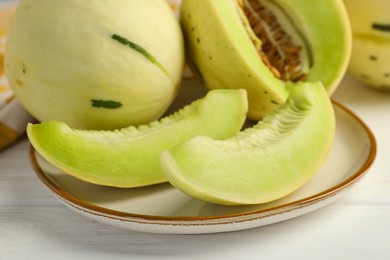 Photo of Fresh whole and cut honeydew melons on white wooden table, closeup