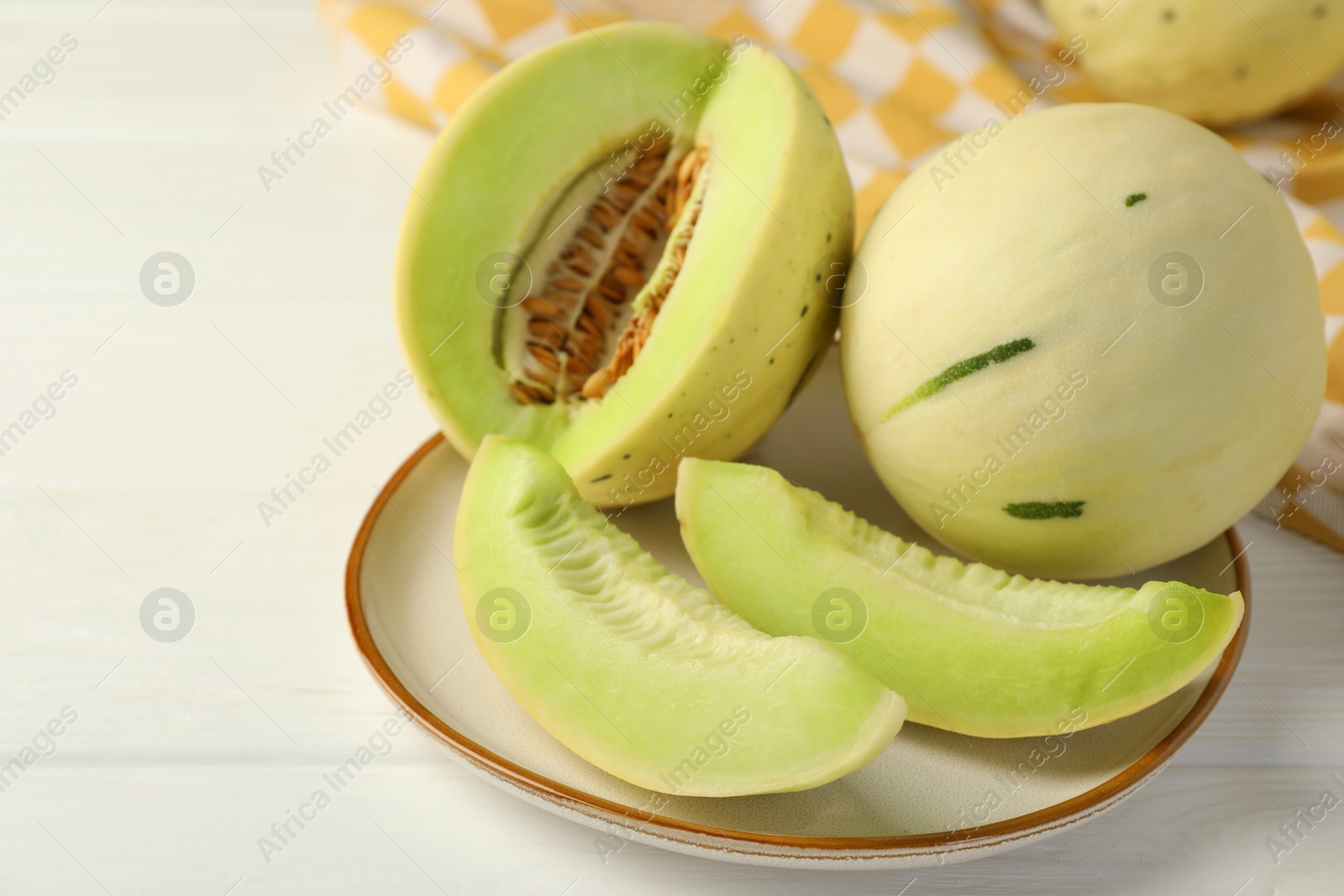 Photo of Fresh whole and cut honeydew melons on white wooden table, closeup