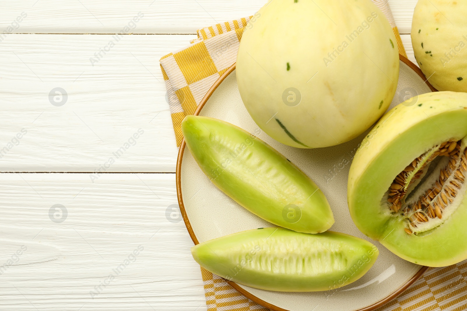 Photo of Fresh whole and cut honeydew melons on white wooden table, top view. Space for text