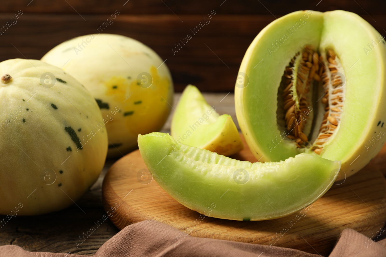 Photo of Fresh whole and cut honeydew melons on wooden table, closeup