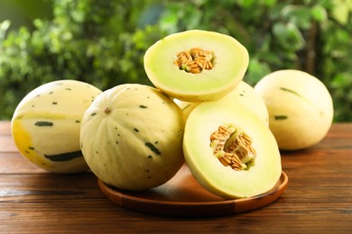 Photo of Fresh whole and cut honeydew melons on wooden table against blurred green background, closeup