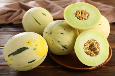 Photo of Fresh whole and cut honeydew melons on wooden table, closeup