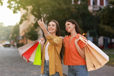 Photo of Happy women with colorful shopping bags taking selfie outdoors