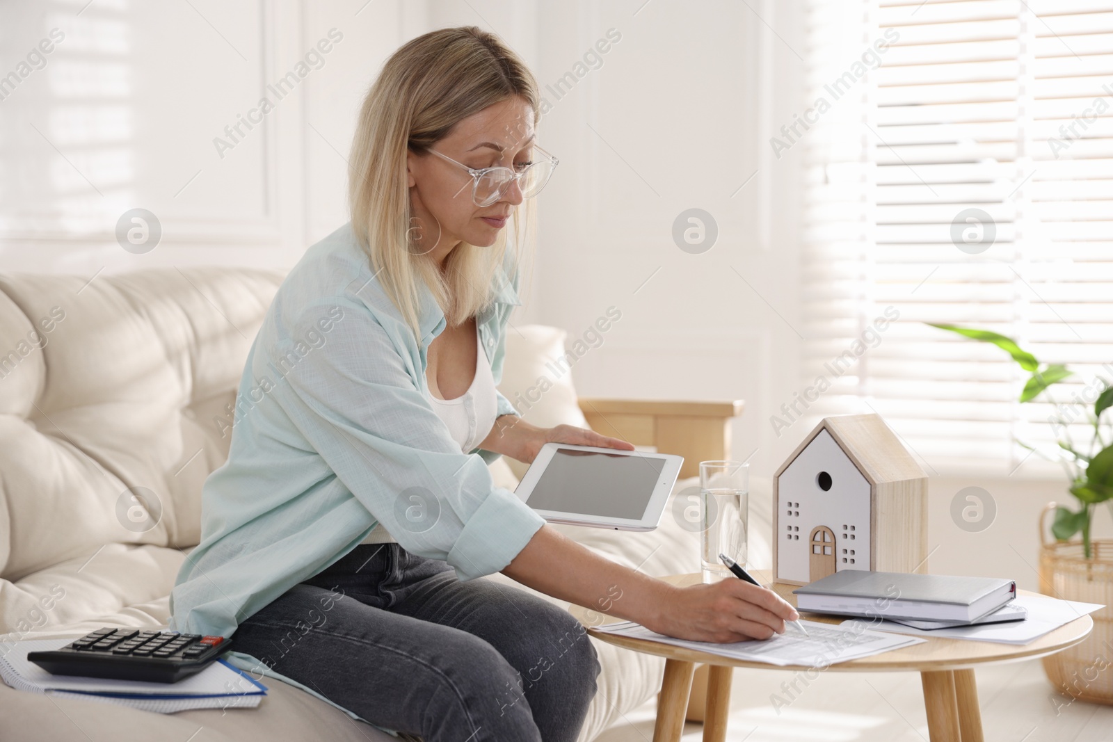 Photo of Budget planning. Woman holding tablet working with accounting document at table indoors