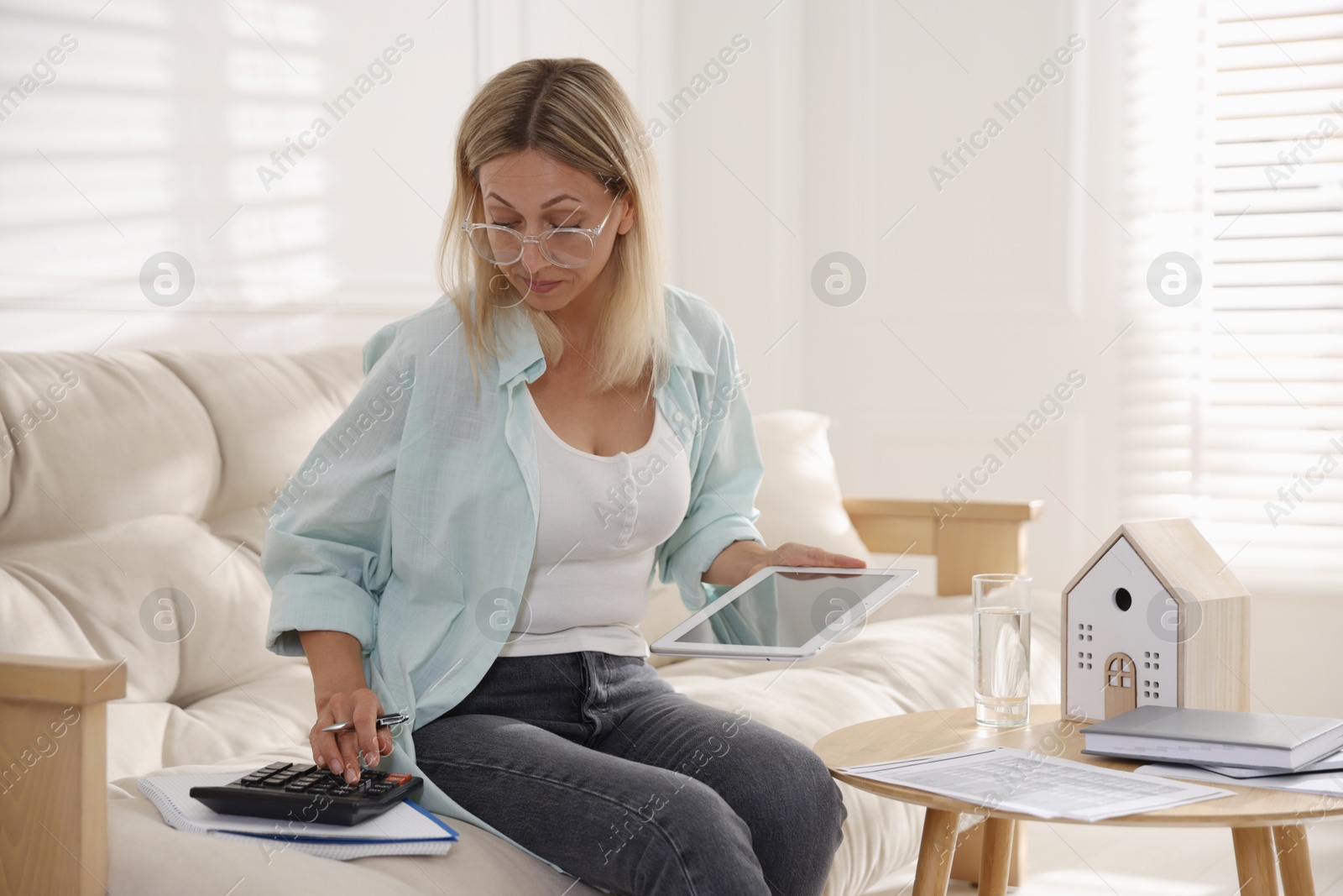 Photo of Budget planning. Woman using calculator and tablet on sofa indoors