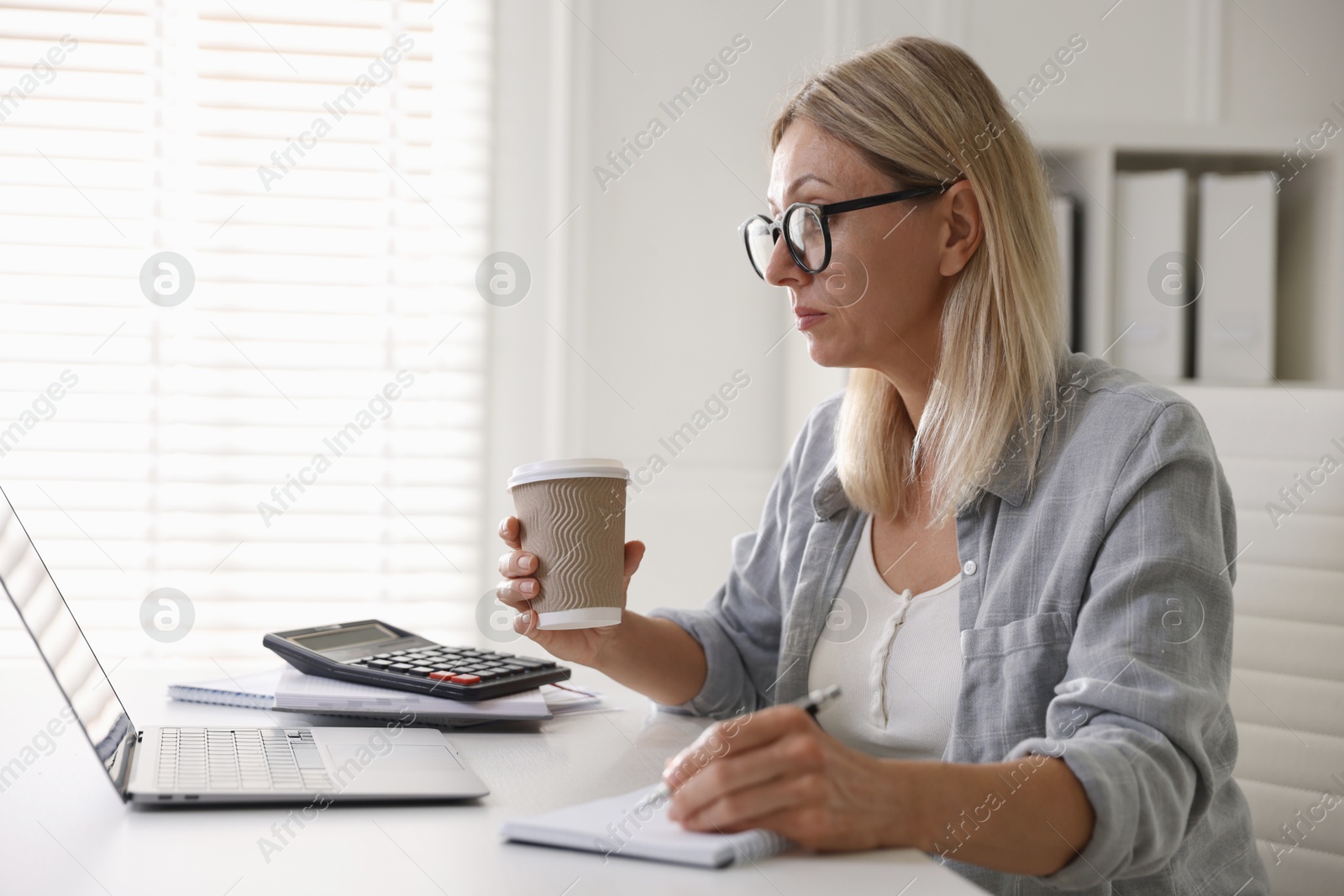 Photo of Budget planning. Woman with coffee taking notes at table indoors