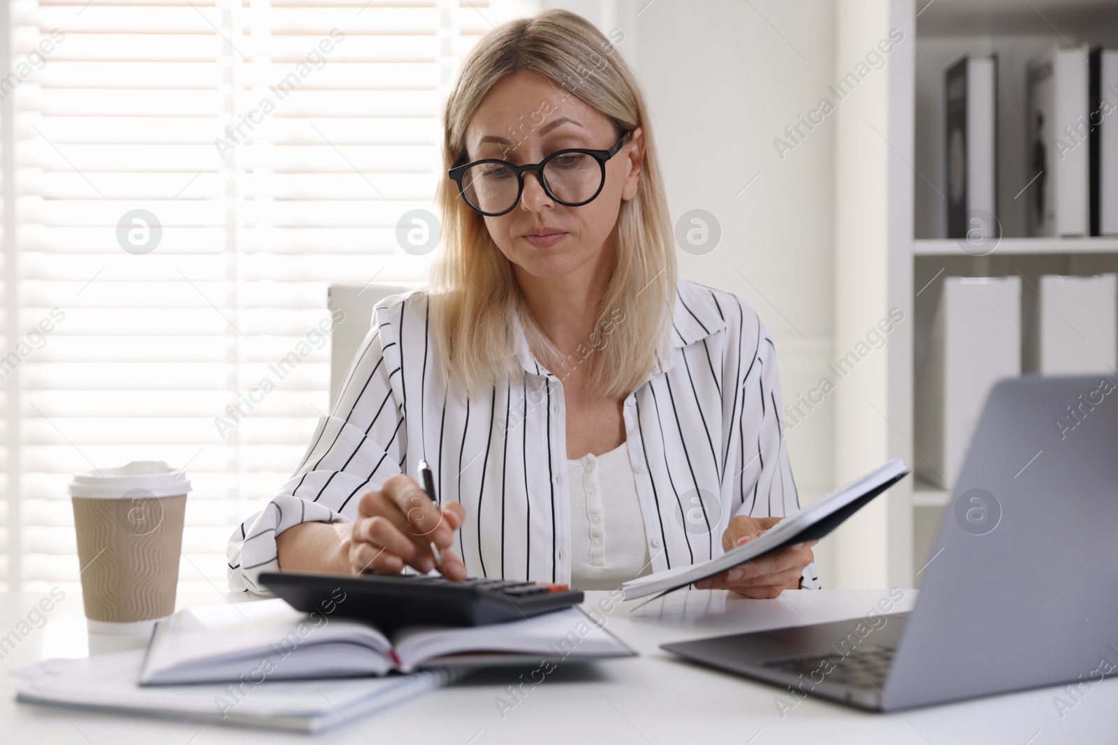 Photo of Budget planning. Woman with notebook using calculator at table indoors