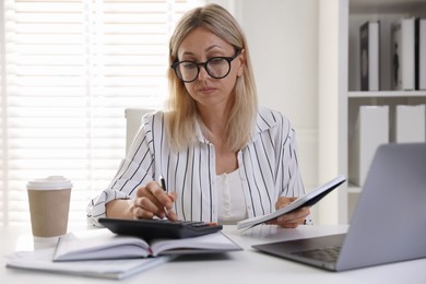 Photo of Budget planning. Woman with notebook using calculator at table indoors