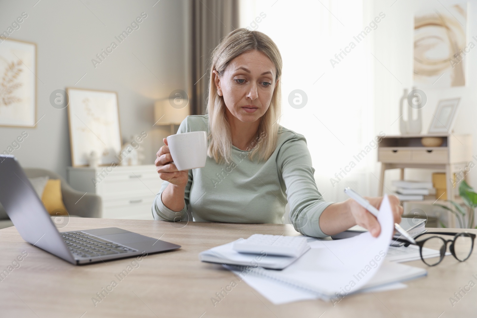 Photo of Budget planning. Woman with cup of drink and document at table indoors