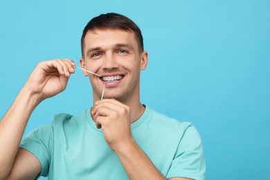 Man with braces cleaning teeth using dental floss on light blue background. Space for text