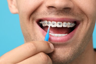 Man with dental braces cleaning teeth using interdental brush on light blue background, closeup