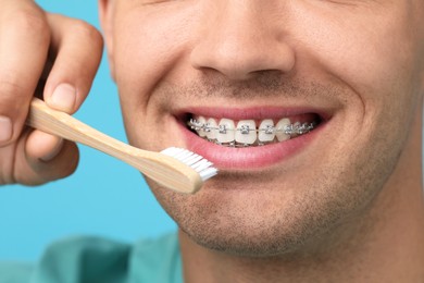 Photo of Man with dental braces cleaning teeth on light blue background, closeup