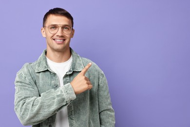 Photo of Smiling man with dental braces pointing at something on violet background. Space for text