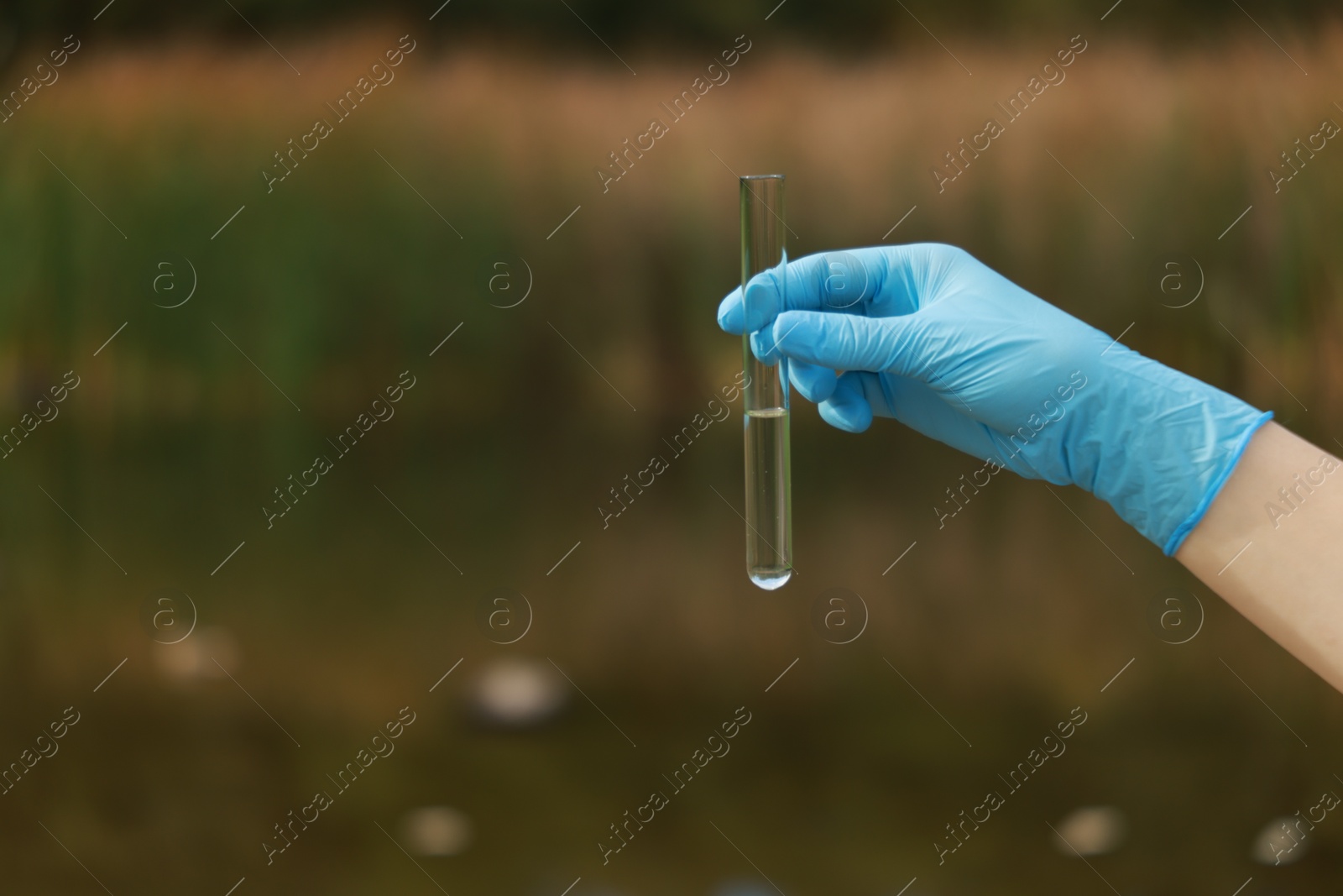 Photo of Examination of water quality. Researcher holding test tube with sample outdoors, closeup. Space for text