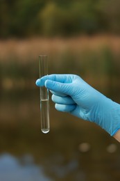 Photo of Examination of water quality. Researcher holding test tube with sample outdoors, closeup