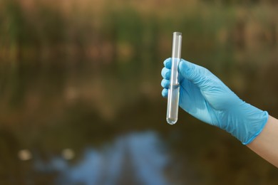 Photo of Examination of water quality. Researcher holding test tube with sample outdoors, closeup. Space for text