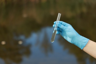 Photo of Examination of water quality. Researcher holding test tube with sample outdoors, closeup. Space for text