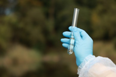 Photo of Examination of water quality. Researcher holding test tube with sample outdoors, closeup. Space for text