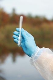 Photo of Examination of water quality. Researcher holding test tube with sample outdoors, closeup