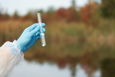 Photo of Examination of water quality. Researcher holding test tube with sample outdoors, closeup. Space for text