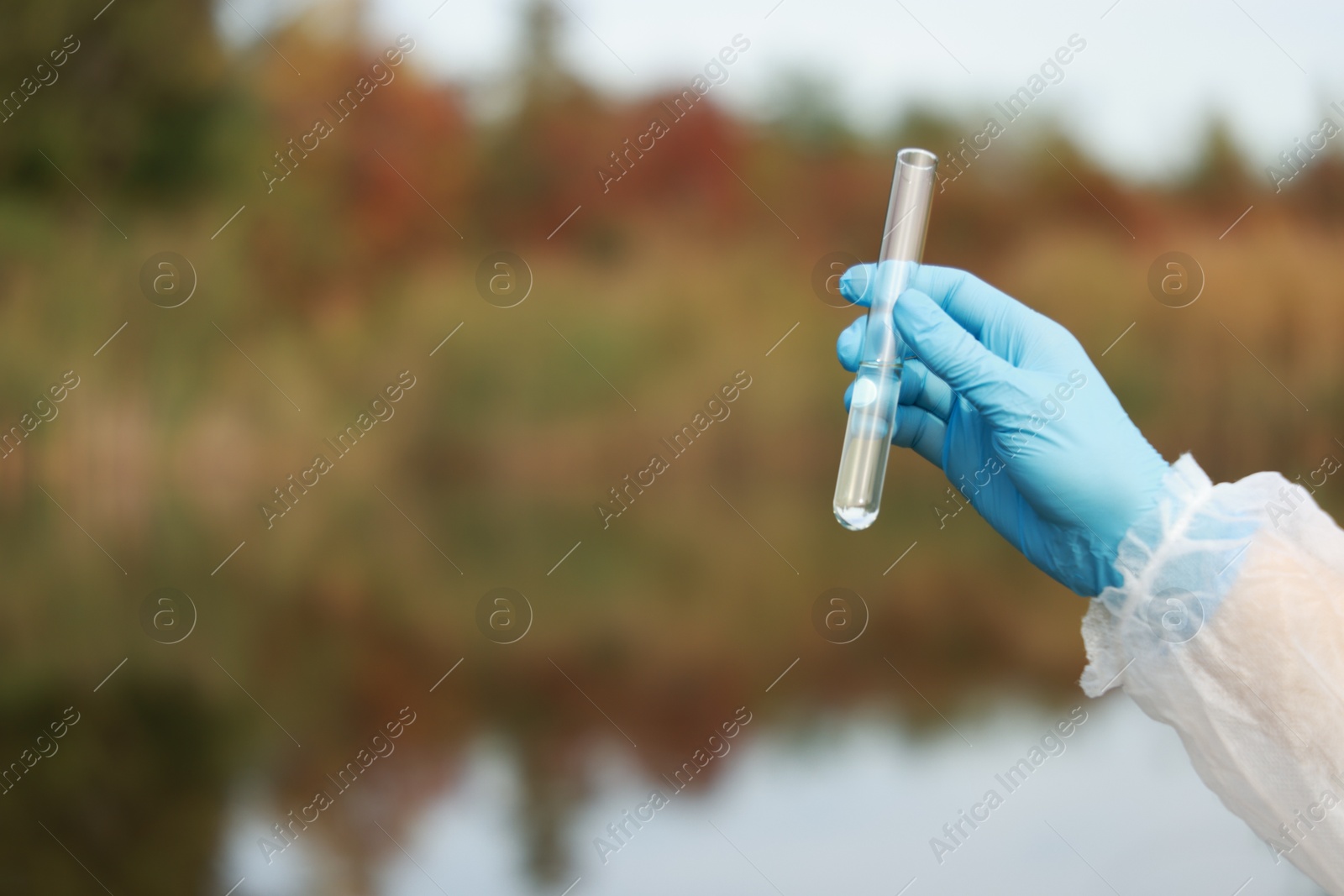 Photo of Examination of water quality. Researcher holding test tube with sample outdoors, closeup. Space for text