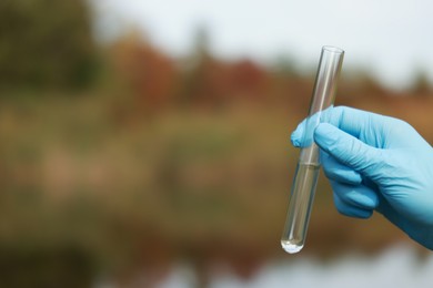 Photo of Examination of water quality. Researcher holding test tube with sample outdoors, closeup. Space for text