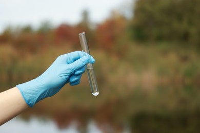 Photo of Examination of water quality. Researcher holding test tube with sample outdoors, closeup. Space for text